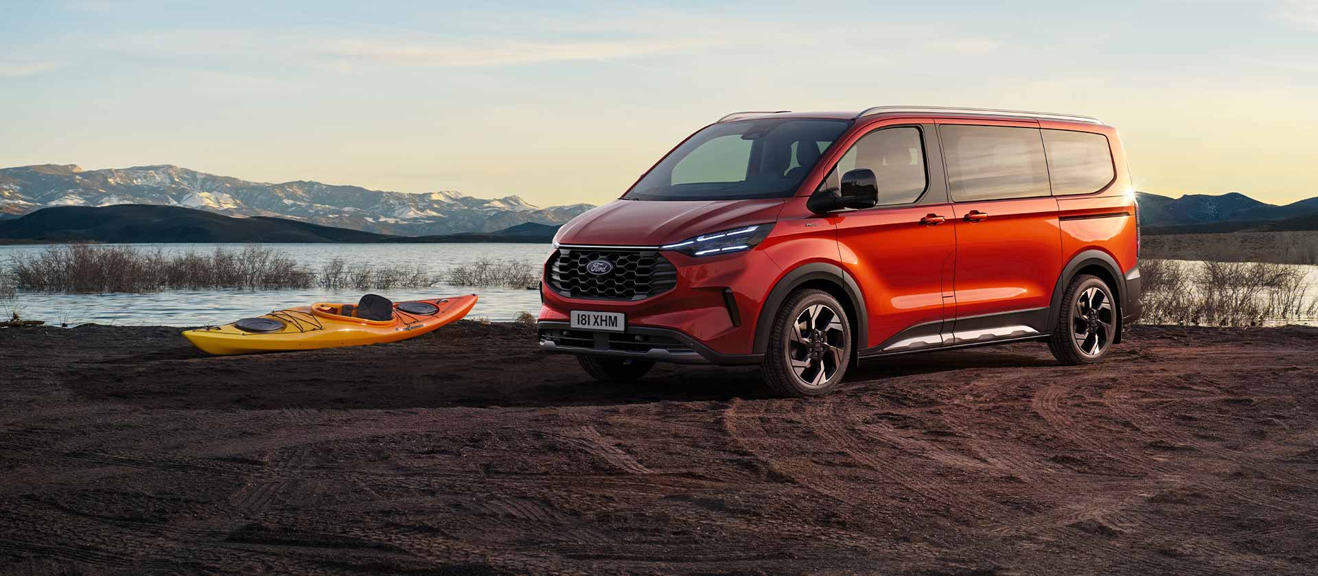 U jezera parkuje červená dodávka Ford Tourneo Custom. Po jezeře pluje kajak. 