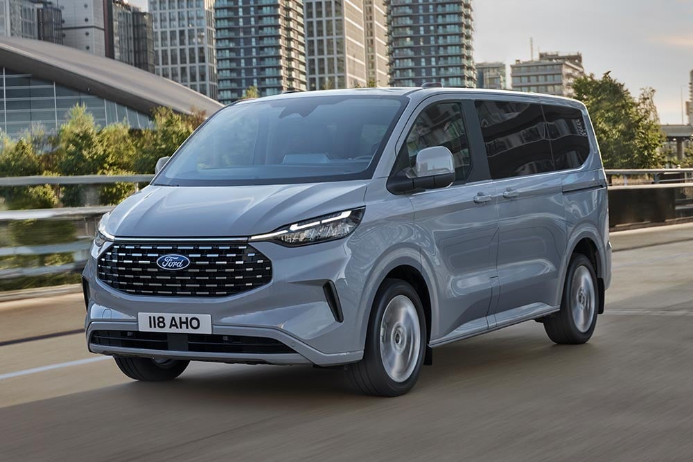 Šedý Ford Tourneo Custom jedoucí po městské silnici.