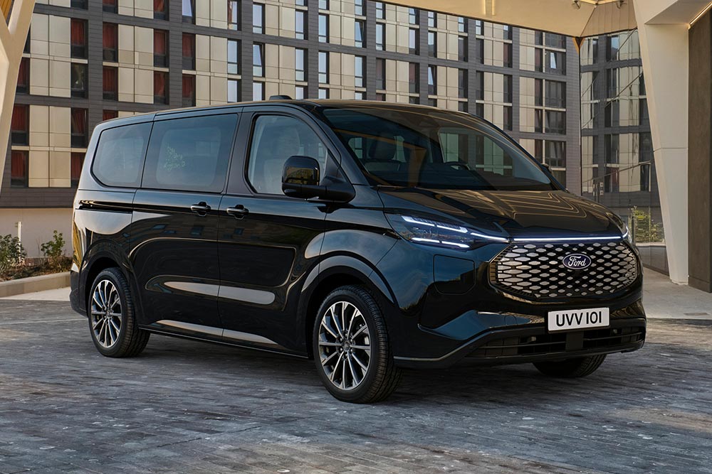 Před moderní budovou parkuje černý Ford E-Tourneo Custom.