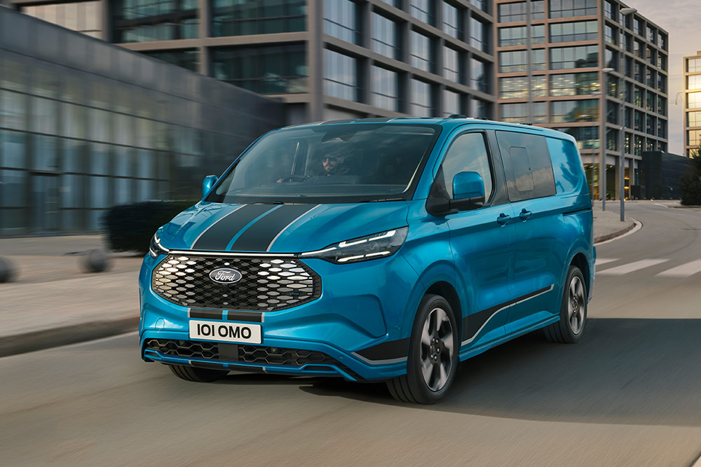 Modrá dodávka Ford E-Transit Custom DCiV Sport jedoucí po ulici ve městě.