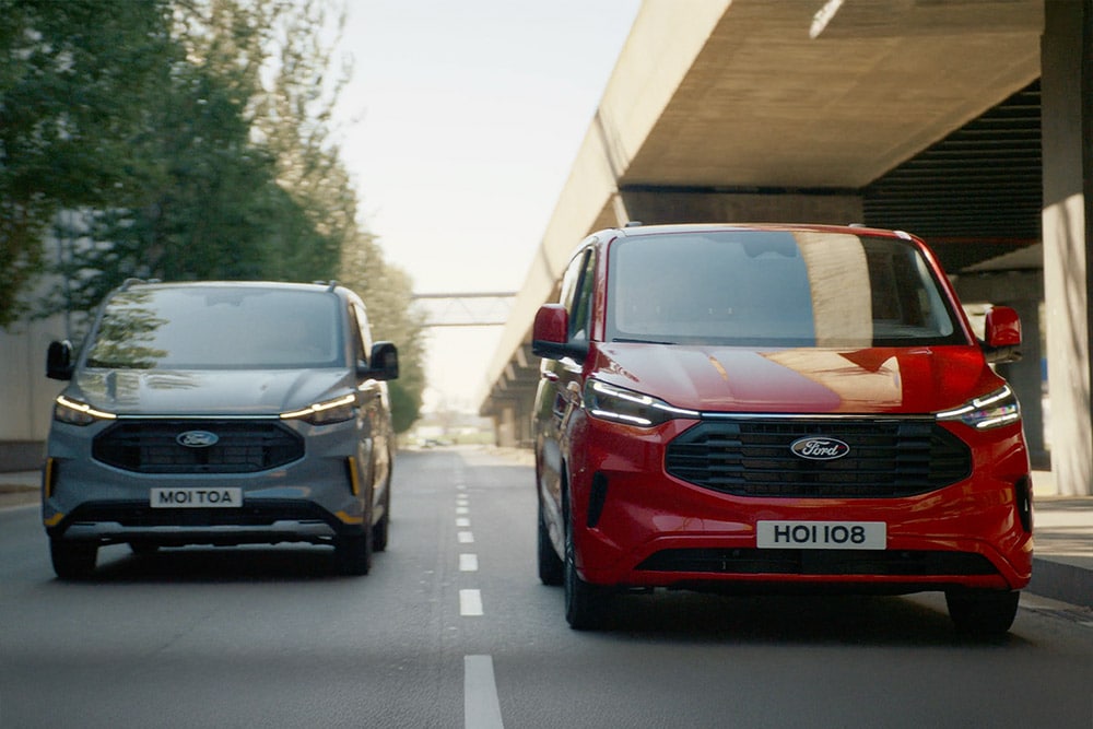 Šedá a červená dodávka Ford Transit Custom jedoucí po silnici.