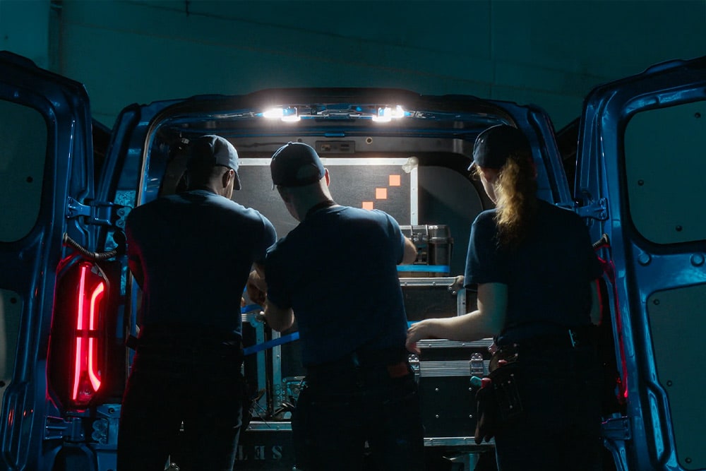 Tři osoby pracující v zadní části elektrické dodávky Ford E-Transit Custom.