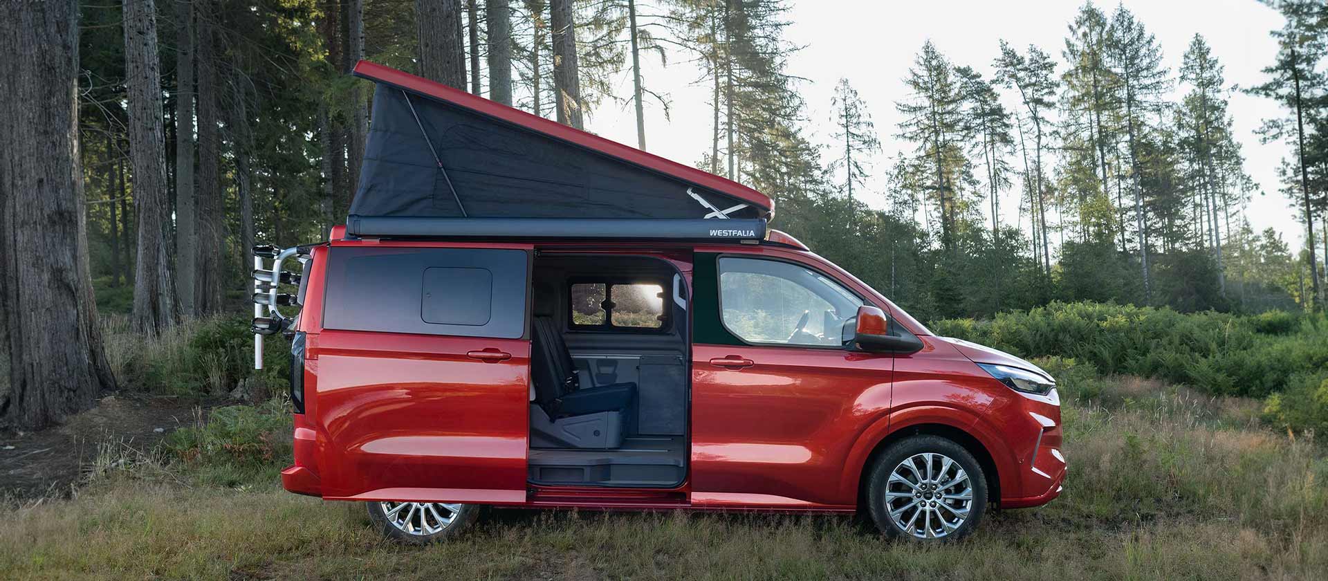 Červený obytný vůz Ford Transit Nugget s výklopnou střechou a otevřenými dveřmi.