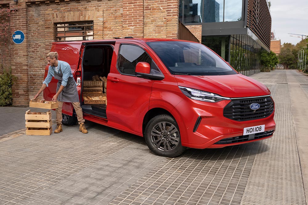 Kurýr nakládá balíky do červeného vozu Ford Transit Custom.