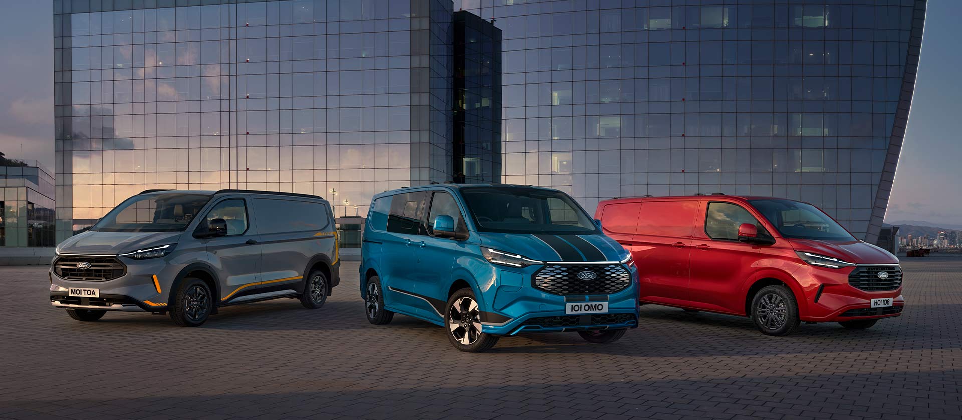 Tři zaparkované dodávky Ford Transit Custom v šedé, modré a červené barvě. 