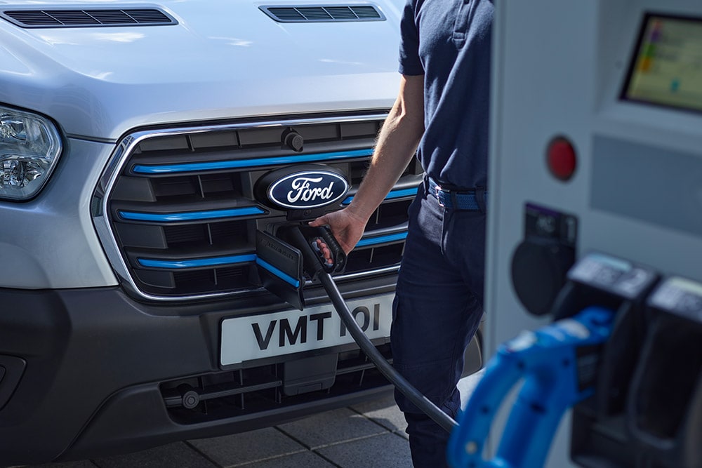 Detailní záběr na nabíjecí port modré elektrické dodávky Ford E-Transit se zapojeným nabíjecím kabelem.
