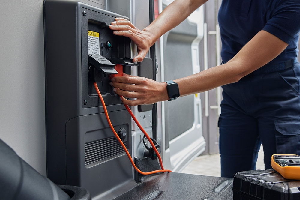 Detailní záběr na osobu zapojující nabíjecí kabel do stříbrné elektrické dodávky Ford E-Transit.