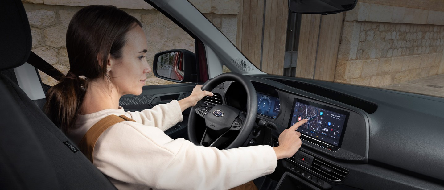 A woman touches the 10” touchscreen while sat in the driver’s seat of All-New Ford Transit Connect.