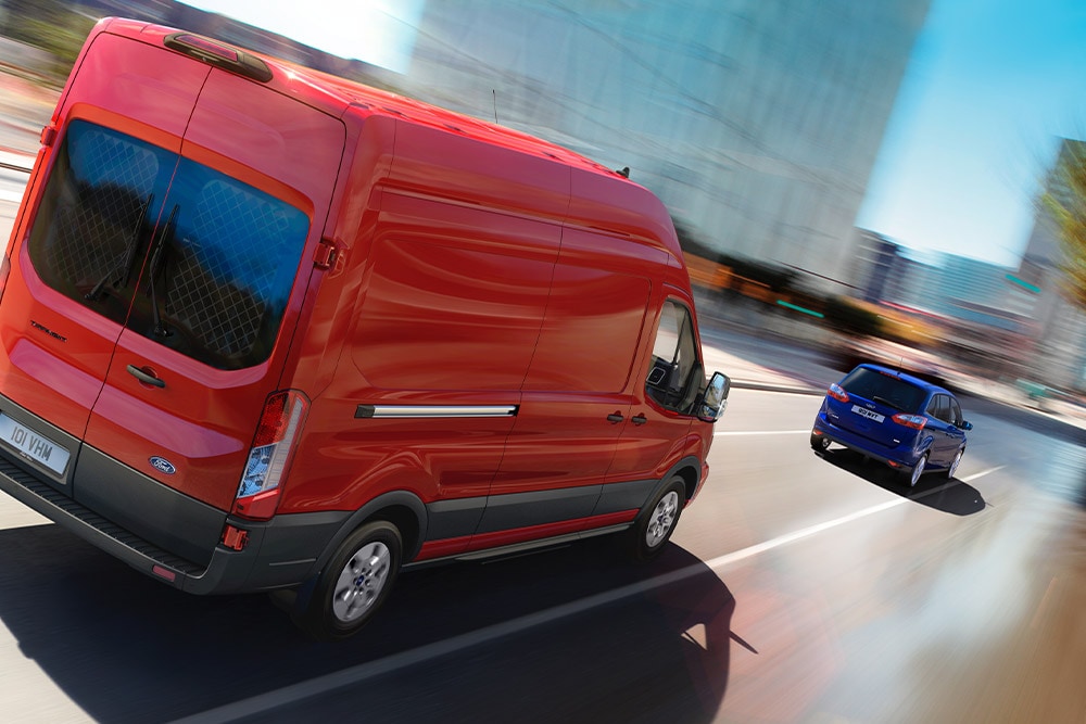Červený Ford Transit Van jedoucí po silnici.