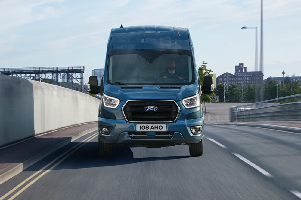 Čelní pohled na modrý Ford Transit Van jedoucí po silnici. 