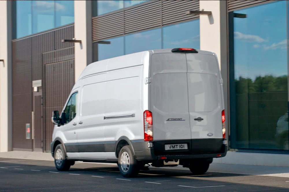 Zadní pohled na stříbrný Ford Transit Van zaparkovaný na městské ulici. 