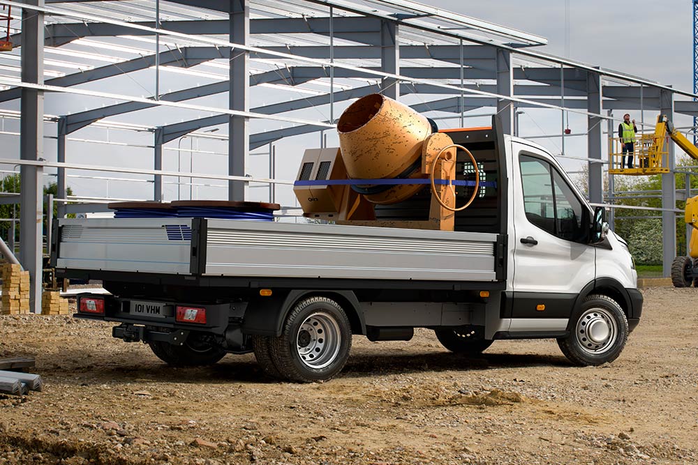 Ford Transit Podvozek s míchačem cementu na ložné ploše zaparkovaný na staveništi. 