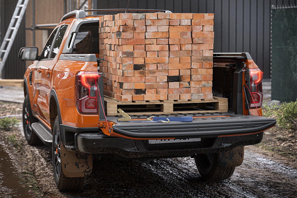 Pohled zezadu na oranžový Ford Ranger s nákladem cihel na ložné ploše.
