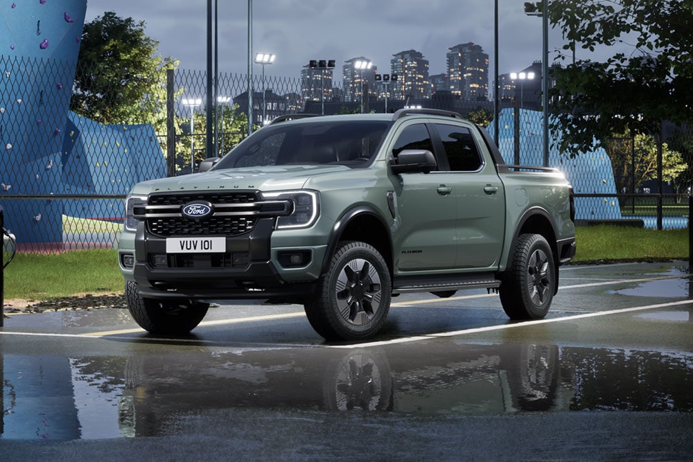 Šedý Ford Ranger PHEV zaparkovaný před panoramatem města za soumraku.