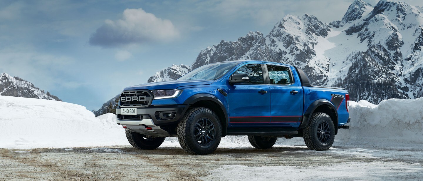 Blue Ford Ranger Raptor driving through a countryside, front three quarter view Blue Ford Ranger Raptor driving through a countryside, front three quarter view