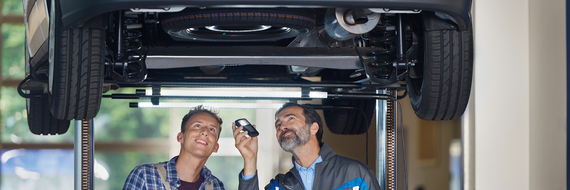 Service employee and customer standing under the car at workshop