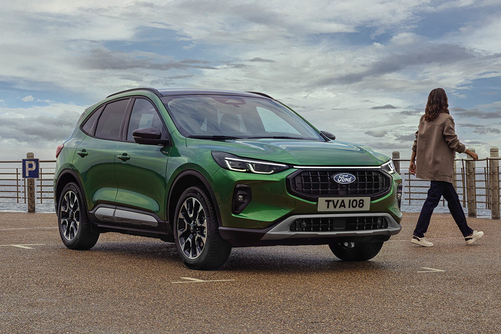Přední 3/4 pohled na zelený Ford Kuga zaparkovaný u pobřežního zábradlí, se dvěma lidmi poblíž.