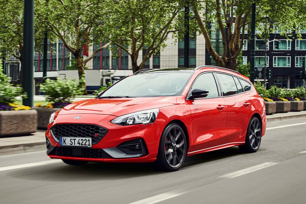 Červený Ford Focus Estate driving na městské silnici z předního tříčtvrtečního úhlu.